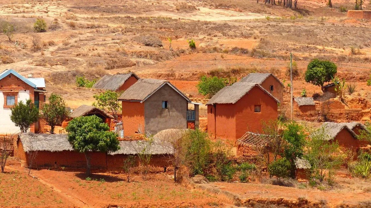 Village traditionnel madagacar avec maisons en terre ocre dispersées dans un paysage aride