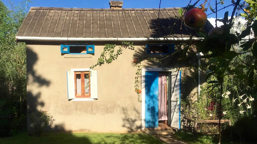 Maison en pierre crépie avec porte bleue et fenêtre ornée de lierre sous un toit en tuiles
