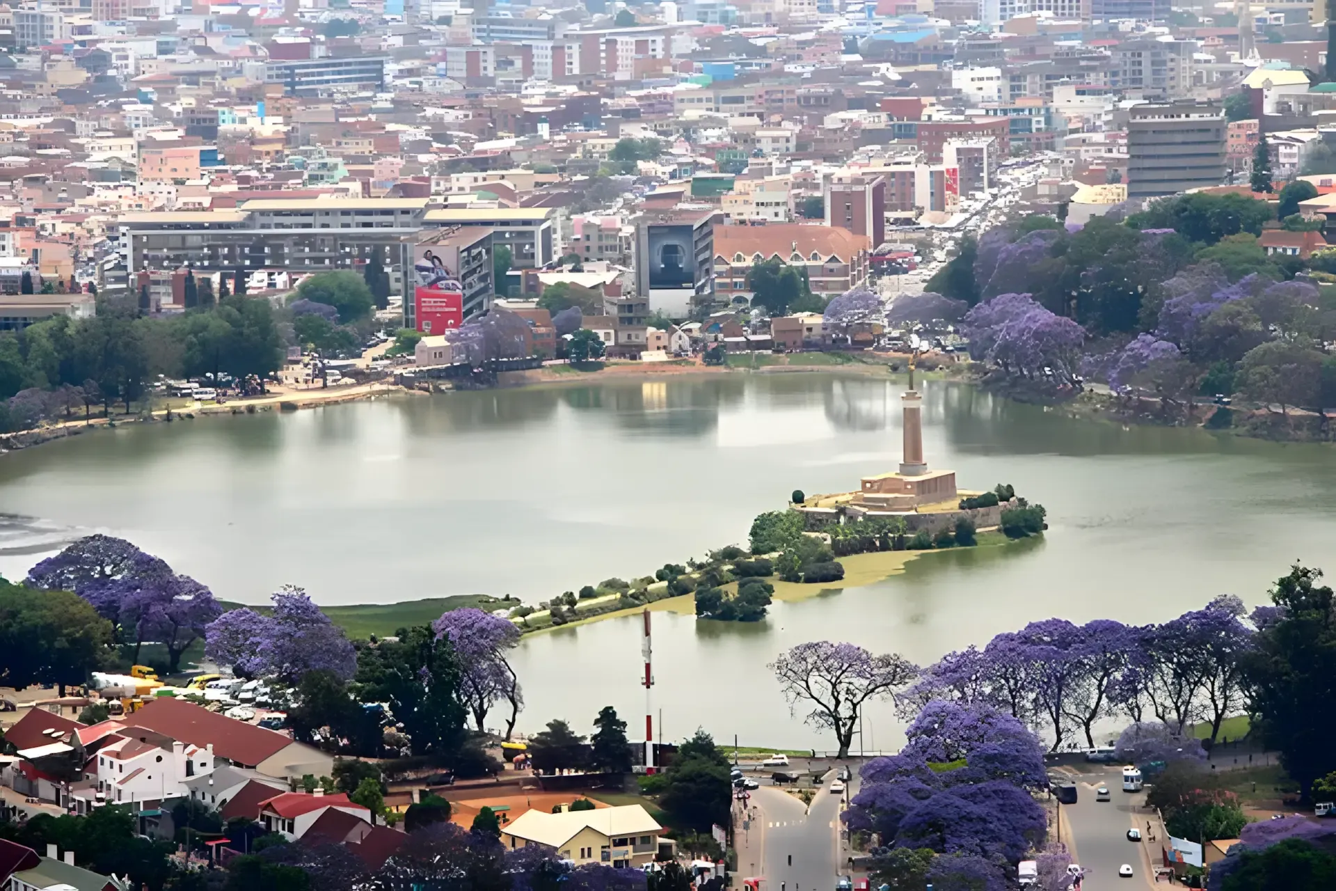 Vue aérienne d’un lac urbain entouré de jardins fleuris à Antananarivo.