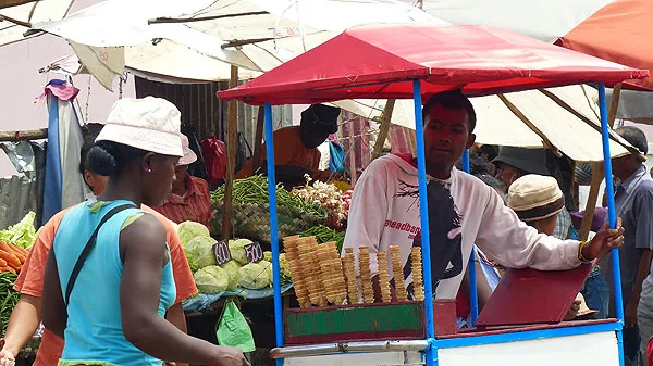 Marché malgache femme en turquoise achetant glaces artisanales sous abri rouge