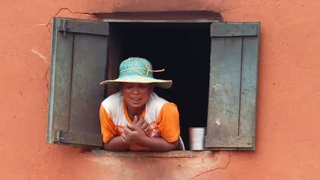 Femme souriante en chapeau de paille penchée à une fenêtre en bois colorée